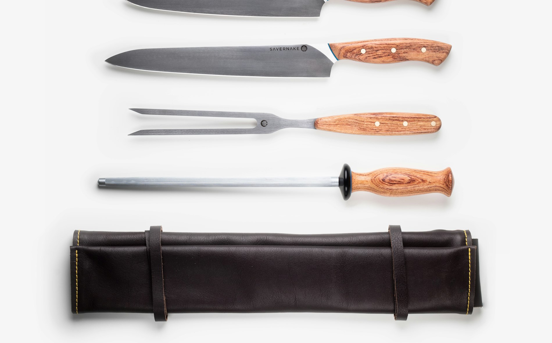 A chef's knife resting on a wooden cutting board beside freshly sliced vegetables.
